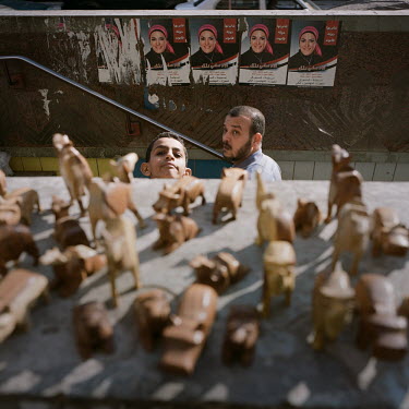 Small wooden sculptures of animals are sold at the entrance to a metro station, with political posters of an election candidate on the wall behind.