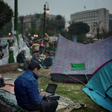 A protestor uses a laptop and mobile phone while siting among protestor's tents in Tahrir Square.
