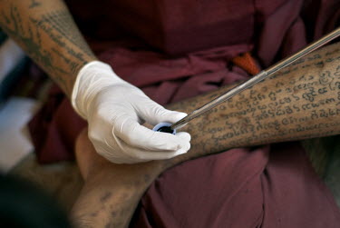 Tattoo master (Khru Sak) Ajarn Kamtawn (now deceased) dips his needle into a jar of ink. He was one of the few masters who still tattooed using the ancient northern Lanna script rather than Khmer deri...