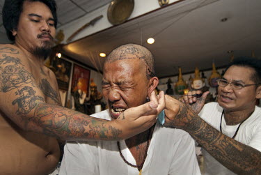 Tattoo master (khru Sak) Ajarn Montri makes a Sak Yan or Sacred Tattoo on the head of a disciple (luuk sit). An assistant has to hold the recipients head as it is a very painful place to be tattooed.
