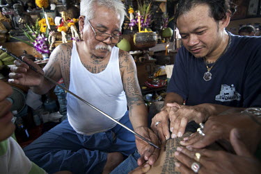 Tattoo master (khru Sak) Ajarn Thong makes a Sak Yan or Sacred Tattoo on a disciple (luuk sit). The metal needle he uses is called a mai sak.