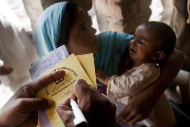 A WHO-sponsored NGO worker fills out an immunization card after giving an injection to a baby in a rural village outside Naushero Feroz.