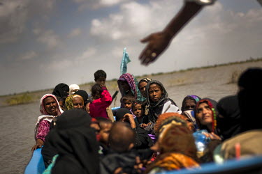 Women and children wait for a boat to ferry them to their village as road access has been cut off by the monsoon floods.