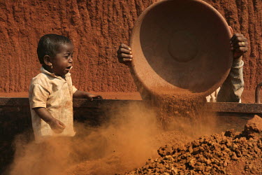 A child watches as a worker dumps a load of rubble into the back of a truck at a stone quarry. Labourers at this site work for around 200 Rupees (GBP 2.5) a day.