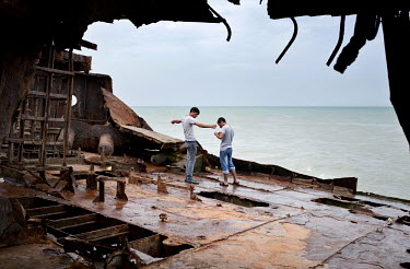 Two young men fishing in the Caspian Sea from the deck of a rusting ship.