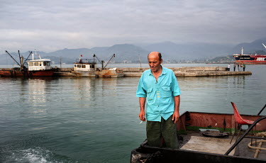 A man smokes a cigarette on the stern of a small boat in Batumi harbour.