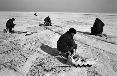 Ice fishermen who have drilled holes into the frozen sea on the Gulf of Finland sit on chairs and boxes, waiting for fish to bite.