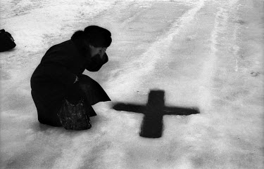 A woman kneels next to a cross cut into the frozen sea during the Feast of Epiphany near St Petersburg on the Gulf of Finland.