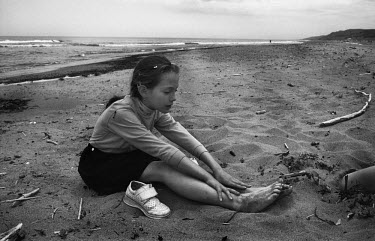 A girls sits on the sand on a beach on the Gulf of Patience on the island of Sakhalin.