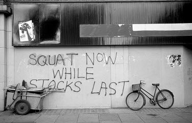 A bicycle and a cleaners trolly by a wall sprayed with pro-squatting graffiti that reads: 'SQUAT NOW WHILE STOCKS LAST', on Westbourne Grove, Notting Hill, London.