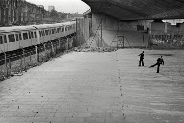 Two boys beneath the Westway flyover (A40) throw stones at a London Underground train as it passes Acklam Road, Notting Hill, London.