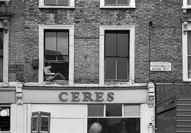 A man sits in a window above the Ceres wholefood shop on Portobello Road, Notting Hill, West London.