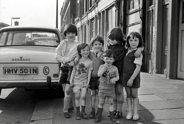 A group of children standing on the pavement on Kensal Road in North Kensington, West London. The borded up houses behind them were soon to be demolished and replaced with a mixture of social housing...