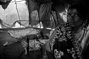 A mother sits near her three year old daughter, who has severe malnutrition and lies naked, on the floor of a makeshift tent in a camp for IDPs (internally displaced persons). The Horn of Africa is cu...