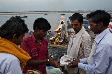 Mourners exchange religious items on the ghats while a body of a relative burns in the background at the Harishchandra Ghat in the ancient city of Varanasi.