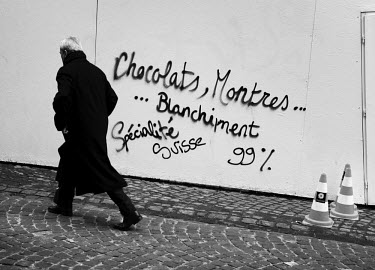A banker passes graffiti left by 'les Indignes' (members of the Occupy movement) 'Chocolate, watches ... money laundering Swiss specialities', on a construction hoarding outside a major bank at the en...