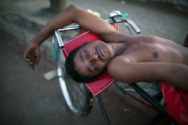 A tricycle rickshaw driver rests on his bike near the docks in Yangon.