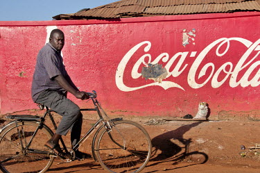 A man cycles past a wall painted with the red and white coca-cola livery.
