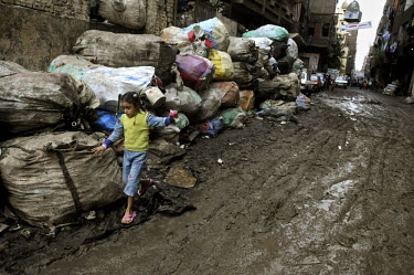 A young girl walks along a road in Mokattam thick with mud and piled, each side, with bags of rubbish. The district is home to the Zabaleen, a minority group of Coptic Christians who have worked as Ca...