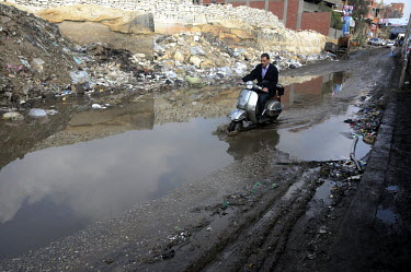 A man wearing a suit rides his scooter through a large puddle, through piles of excess rubbish in Mokattam a district that is home to many Zabaleen, a minority group of Coptic Christians who have work...