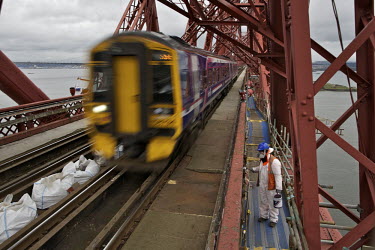 A train travels past as workers wait, after a klaxon was sounded so they had time to get out of the way, on the 125 year old Forth Rail Bridge which spans the river Forth near Edinburgh. Network Rail,...