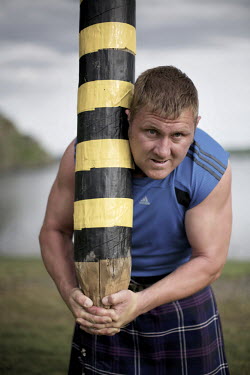 Neil Elliott wears a kilt and holds a caber near his home in Dumbarton. He competes in over 40 Highland Games and heavyweight events across the world throughout the summer.