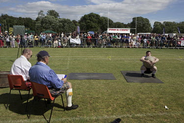 Men judge a man competing in the stone lifting event at Helensburgh and Lomond Highland games, Argyl and Bute.