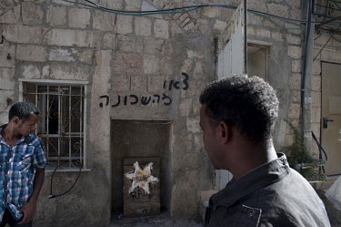 Men outside a building, home to dozens of Eritrean asylum seekers, which was set on fire by a local resident early morning in Jerusalem. The Hebrew writing on the wall reads ^get out of the neighborho...