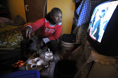 A woman pours coffee as she watches TV, sitting at her room in a compound of Eritrean asylum seekers.