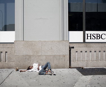 A young man lies passed out on a sidewalk next to a bank in Chelsea, New York City.