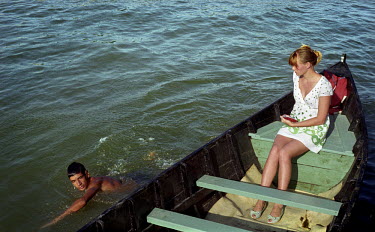 A woman sits in a boat as a boy swims past.