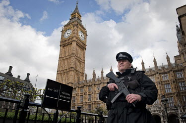 An armed police officer in front of The House of Commons and The Clock Tower in Westminster, London. Although the tower is popularly referred to as Big Ben, this is actually the nickname of the bell h...