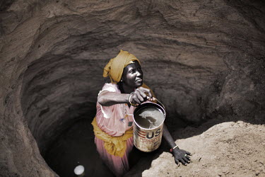 A woman hands up an empty US AID container of water from a well dug in Jammam refugee camp. With waiting times at the official water points taking up to six hours camp dwellers have taken to digging t...