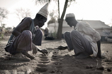 Two elderly men playing a game, possibly Mancala, on the dusty ground in Doro refugee camp.