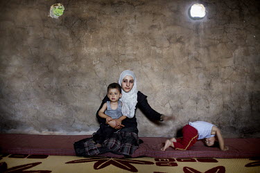 A woman and her children sit inside a concrete storage room that is home to several Syrian women and their children who have fled over the border to escape the fighting in their homeland. Inside the r...