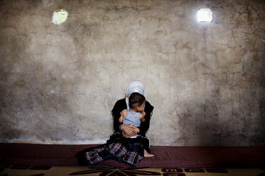 A woman sits with her child inside a concrete storage room that is home to several Syrian women and their children who have fled over the border to escape the fighting in their homeland. Inside the ro...