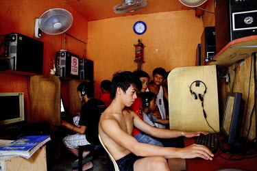 Young boys sit at computers in a cybercafe. It is so hot that one boy sits in just his shorts