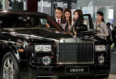 A Rolls Royce Motor Cars Ltd representative shows the features of a Phantom automobile to a group of female visitors during the China ( Guangzhou) International Automobile Exhibition. Despite signs of...