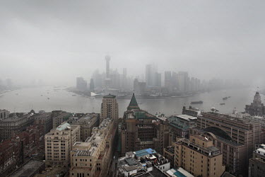 The historic Bund waterfront facing, on the far bank of the Huangpu River, the smog draped district of Pudong and the Lujiazui Finance and Trade Zone. Rising into the fog is the Pearl Tower (bulbous b...