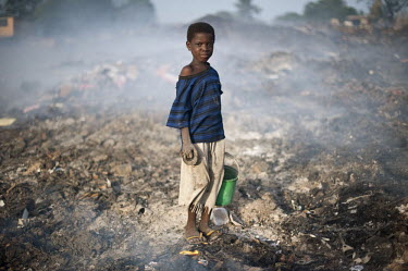 A young girl sifting through a smoking rubbish dump near Old Fadama, a squatter settlement colloquially referred to as 'Sodom and Gomorrah',  searching for scrap metal to sell.