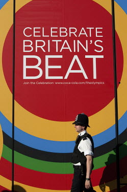 A policeman walks past a Coca-Cola advertisement on the way to a technical rehearsal for the Olympic Opening Ceremony for the 2012 Olympic Games, at the Olympic Stadium, London.