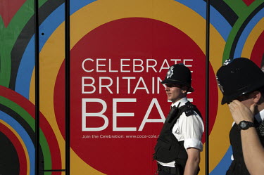 Two policemen walk past a Coca-Cola advertisement on the way to a technical rehearsal for the Olympic Opening Ceremony for the 2012 Olympic Games, at the Olympic Stadium, London.