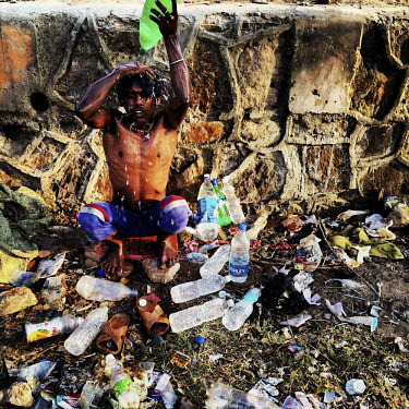 A young man bathes with a plastic bottle he has filled with water from a nearby water tanker. Trash is littered everywhere in Urdu Park where hundreds of street people live.