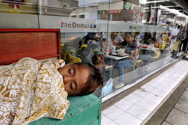Street child sleeping outside a McDonald's franchise in this southern city as middle class consumers eating inside look on.