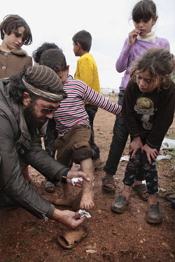 A man tries to clean the muddy feet of a child, a kind but futile gesture, in the Atma refugee camp set right against the Turkish border. The conditions at the camp are rapidly deteriorating as rain has made the ground thick with mud and water and food shortages add to the misery. <brProtests against the regime of Bashar al-Assad erupted in March 2011. Although initially peaceful, they were violently repressed by the Syrian army and police. In response to being ordered to shoot unarmed civilians, large numbers of men deserted and formed the core of the Free Syrian Army (FSA) which was soon joined by civilian volunteers. Since early 2012 the protest movement has escalated into an armed uprising that many consider a civil war. Sustained fighting is ongoing throughout Syria between the regular army and its allied militias and the Free Syrian Army as well as other anti-regime groups, some of which include foreign jihadists.