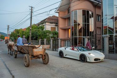 An old fashioned horse drawn cart passes a white Ferrari parked in front of a new glass fronted house on a street in Certeze. The owner of the car is a successful entrepreneur who lives in Paris and h...