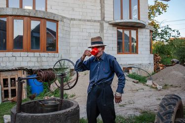 Iacob Berende drinks a cup of water from the well behind his children's newly built home which is still under construction. His children have gone to the UK to work. Most people from this village used...
