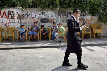 An ultra-orthodox man walks past children of the Ghawi family who are sitting outside their former home in East Jerusalem. The Ghawi and Hanoun families were evicted from their homes on 2 August 2009,...