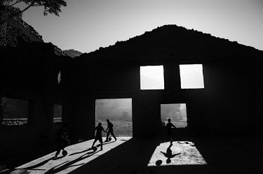 The sun shines through the ruins of an old house, destroyed during the 1990s civil war, where children play a game of football.