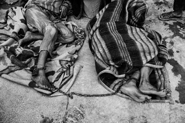 Mental health patients lie on the floor, wrapped in blankets and chained together.